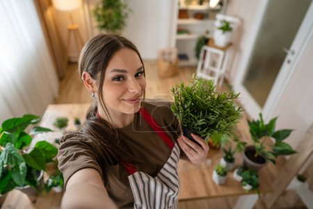 Téléchargez les photos : Une femme jeune femme caucasienne debout à la maison tenir fleurs plantes pot heureux sourire autoportrait UGC User Generated Content vue de face jardinage et botanique horticulture soins concept copier l'espace - en image libre de droit