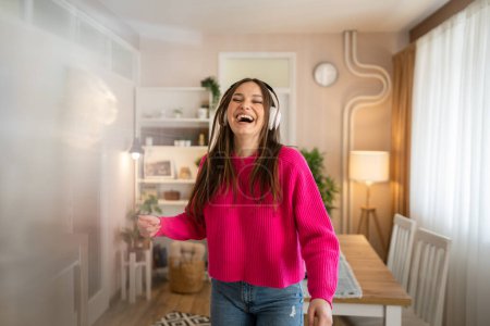 Foto de One woman young caucasian female teenager dancing alone at home with headphones on her head having fun while listen to the music happy smile real people copy space - Imagen libre de derechos