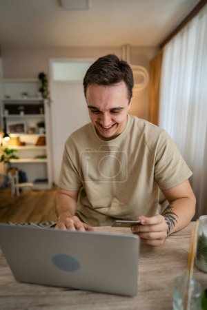 Photo for One man adult caucasian male sit at home happy smile at laptop computer hold bank credit card online shopping concept real people copy space e-commerce - Royalty Free Image