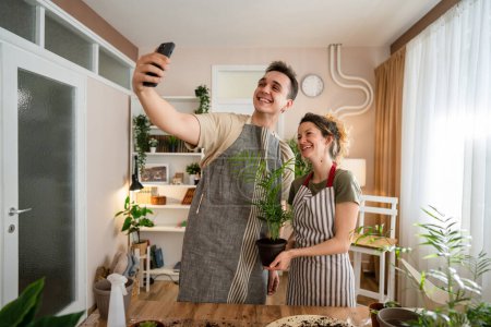 Téléchargez les photos : Couple caucasien homme et femme femme femme et mari plantation de fleurs ensemble prendre soin de plantes à la maison personnes réelles la vie domestique concept de jardinage familial prendre selfie photo avec smartphone copier l'espace - en image libre de droit