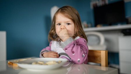 Photo for One girl small caucasian toddler female child eat at the table at home - Royalty Free Image