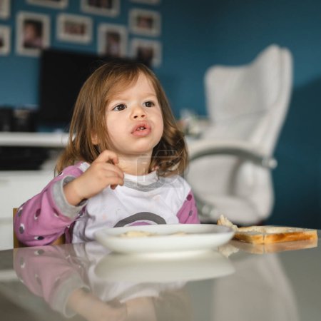 Téléchargez les photos : Une fille petit caucasien tout-petit femelle enfant manger à la table à la maison - en image libre de droit