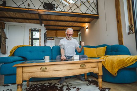 Téléchargez les photos : Un homme heureux homme caucasien âgé avec la barbe en bonne santé célébrer utiliser appareil de pression artérielle pour vérifier et mesurer les résultats tout en s'asseyant à la table à la maison seul les gens réels copier espace concept de soins de santé - en image libre de droit