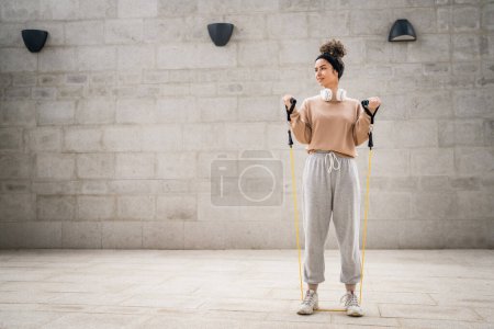 Téléchargez les photos : Une femme adulte caucasienne athlète entraînement féminin avec élastique bandes de résistance en caoutchouc tubes en plein air dans la ville sur fond de béton étirement dans heureux brune santé et fitness concept copier espace - en image libre de droit
