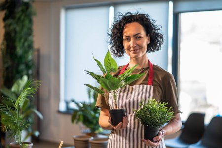 Téléchargez les photos : Une femme mature caucasienne femelle se tenir à la maison avec des plantes de fleurs pot heureux sourire tour de taille vue de face jardinage et botanique horticulture soins concept copier l'espace - en image libre de droit