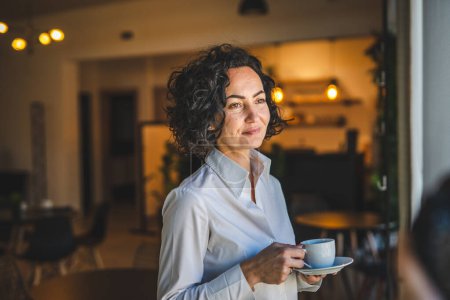 Photo for One woman stand at the window at home or office businesswoman entrepreneur wear white shirt having cup of coffee happy smile real people copy space morning routine mature caucasian female - Royalty Free Image