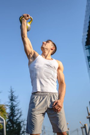 Téléchargez les photos : Un homme jeune athlète musculaire masculin caucasien debout en plein air dans l'entraînement de jour avec cloche russe girya kettlebell poids exercice force et conditionnement endurance personne réelle copier l'espace - en image libre de droit
