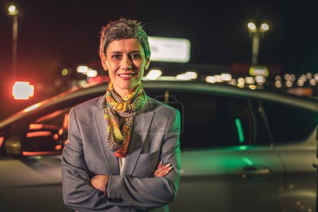 Photo for Portrait of one senior woman modern mature caucasian female with gray short hair stand in the city at night in front of the car real person copy space waist up - Royalty Free Image