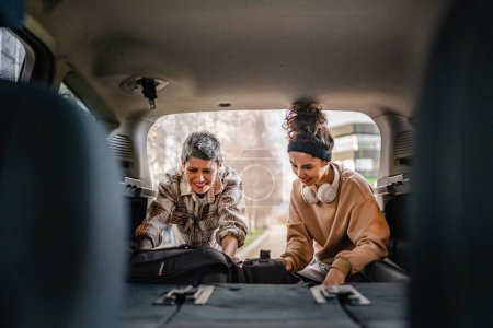 Photo for Two beautiful women student mother and daughter female travel concept take luggage baggage suitcase and other stuff belongings from back of car while moving into dormitory on college campus or travel - Royalty Free Image