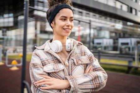 Photo for One woman young adult generation z caucasian modern female with headphones happy smile stand in the city real person copy space in autumn or spring day - Royalty Free Image