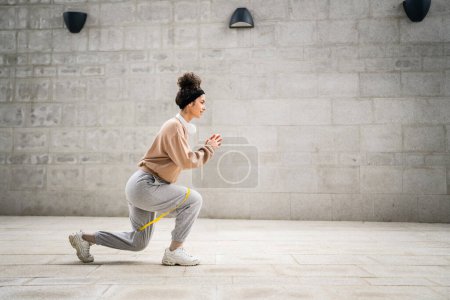 Foto de Una mujer adulta caucásica atleta entrenando con bandas elásticas de goma en exteriores en la ciudad sobre fondo de hormigón estirándose en feliz morena salud y fitness concepto de espacio de copia - Imagen libre de derechos