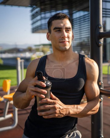 Photo for One caucasian man young male athlete take a brake during outdoor training in the park outdoor gym hold supplement shaker in hand happy confident strong copy space - Royalty Free Image