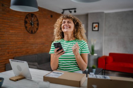 Photo for One caucasian woman use smart phone to check shipping details of the received package online shopping product arrived stand with smartphone app application check online details happy smile - Royalty Free Image