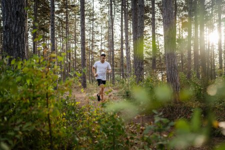 Téléchargez les photos : Un homme jeune athlète homme caucasien courir à travers les bois dans la nature jogging en plein air en automne ou en été jour sport fitness et loisirs mode de vie sain concept personnes réelles copier l'espace - en image libre de droit