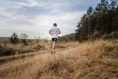 Téléchargez les photos : Un homme jeune athlète homme caucasien courir dans la nature en plein air sur la route de terre jogging en automne ou en été jour sport fitness et loisirs mode de vie sain concept personnes réelles copier l'espace - en image libre de droit