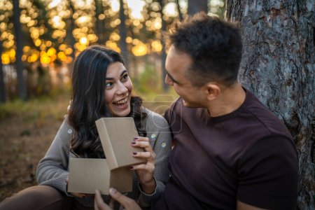 Photo for Two people young adult caucasian man and woman couple boyfriend and girlfriend or husband and wife give gift box present while sit in nature forest park celebrate romantic love real people copy space - Royalty Free Image