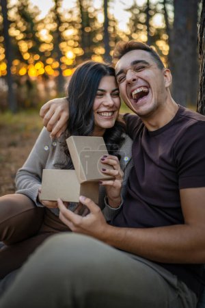 Photo for Two people young adult caucasian man and woman couple boyfriend and girlfriend or husband and wife give gift box present while sit in nature forest park celebrate romantic love real people copy space - Royalty Free Image