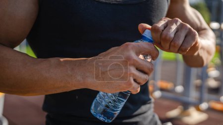 Téléchargez les photos : Un homme caucasien athlète masculin tenir bouteille en plastique de l'ouverture de l'eau et se préparer à boire tout en s'entraînant en plein air dans l'hydratation du jour ensoleillé et un mode de vie sain concept copier l'espace - en image libre de droit
