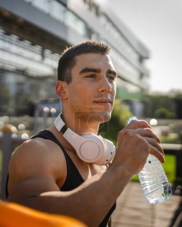 Téléchargez les photos : Un homme caucasien athlète masculin tenir bouteille en plastique de l'ouverture de l'eau et se préparer à boire tout en s'entraînant en plein air dans l'hydratation du jour ensoleillé et un mode de vie sain concept copier l'espace - en image libre de droit