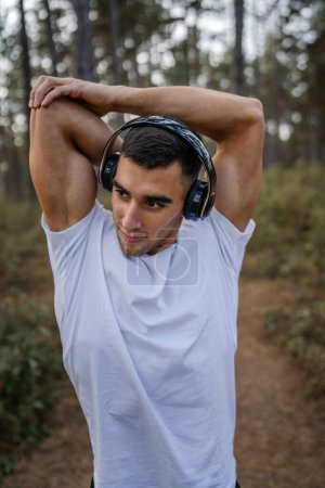 Téléchargez les photos : Un homme jeune athlète homme caucasien étirement dans les bois dans la nature en plein air jogging ou exercice en automne ou en été jour sport fitness et loisirs mode de vie sain concept personnes réelles copier l'espace - en image libre de droit