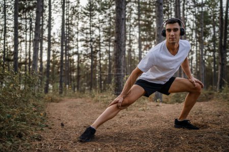 Photo for One man young caucasian male athlete stretch in the woods in nature outdoor jogging or exercise in autumn or summer day sport fitness and recreation healthy lifestyle concept real people copy space - Royalty Free Image