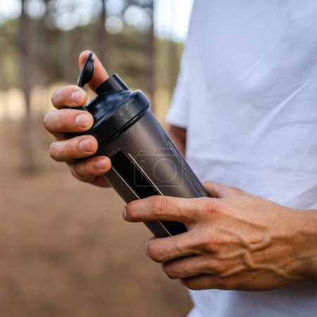 Photo for One caucasian man young male athlete take a brake during outdoor training in the park outdoor in the forest or woodland in nature hold supplement shaker in hand happy confident strong copy space - Royalty Free Image