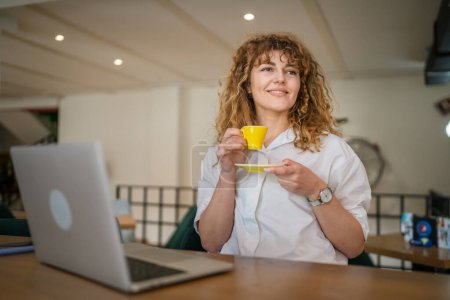 Foto de Una mujer caucásica adulta con sonrisa de pelo rizado tomando una taza de café en la cafetería sin preocupaciones disfrutar de espacio de copia sonriente feliz - Imagen libre de derechos