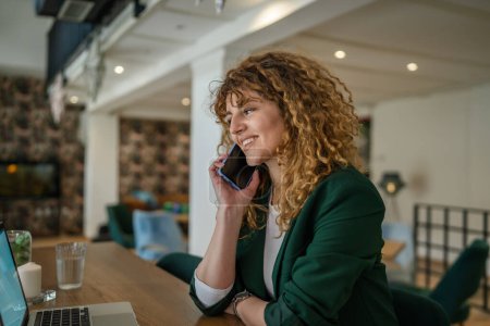 Foto de Una mujer adulta caucásica hembra sentarse en el trabajo de la cafetería en el ordenador portátil hacer una llamada telefónica hablar sonrisa feliz confiado sonriendo espacio de copia en persona real - Imagen libre de derechos