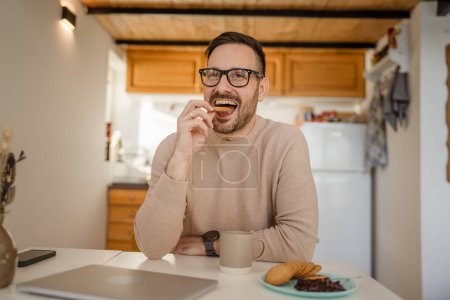 Photo for One adult man caucasian old male sit at a table at home putting jam on a biscuit preparing to eat breakfast enjoy snack relaxed in his home environment real person copy space daily routine - Royalty Free Image
