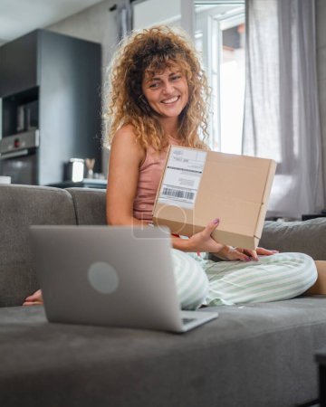 Foto de Una mujer caucásica mujer adulta recibe regalos en caja abierta leer tarjeta sonrisa feliz delante de la computadora portátil en casa tener videollamada en línea - Imagen libre de derechos