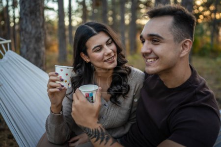 Photo for Young couple man and woman boyfriend and girlfriend or husband and wife in love relationship hold paper cup of coffee or tea while spend time together in the park forest bonding love real people - Royalty Free Image
