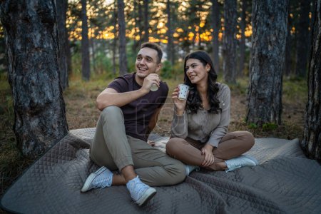 Photo for Young couple man and woman boyfriend and girlfriend or husband and wife in love relationship hold paper cup of coffee or tea while spend time together in the park forest bonding love real people - Royalty Free Image
