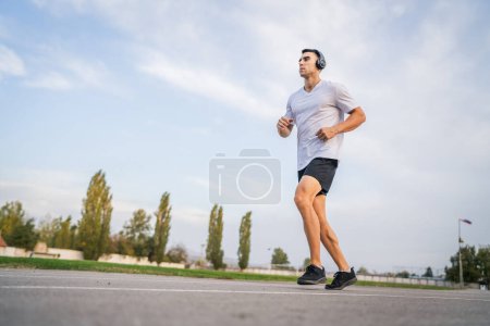Téléchargez les photos : Adulte homme caucasien jogging sur la piste de course athlète masculin dans l'entraînement du stade courir au printemps ensoleillé ou jour d'été de vraies personnes concept de mode de vie sain - en image libre de droit