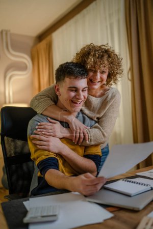 Photo for Young man and his mother woman hold paper read good news in letter sit at desk at home beautiful female received correspondence bank statement or notification invitation scholarship pleasant message - Royalty Free Image