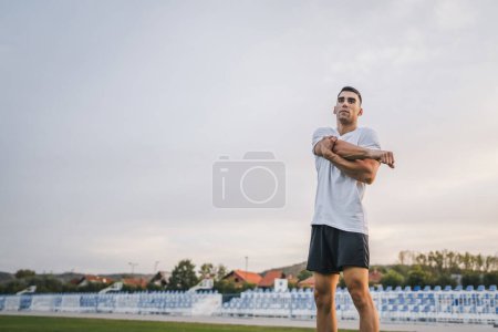 Photo for One man young caucasian male athlete stretch outdoor at stadium track jogging or exercise in autumn or summer day sport fitness and recreation healthy lifestyle concept real people copy space - Royalty Free Image