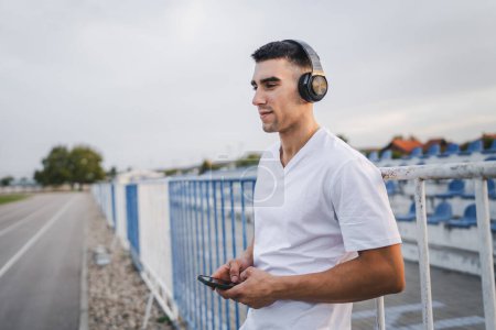 Photo for Portrait of an athlete using mobile phone during morning run Athletic man listening to music on headphones use mobile phone app application - Royalty Free Image