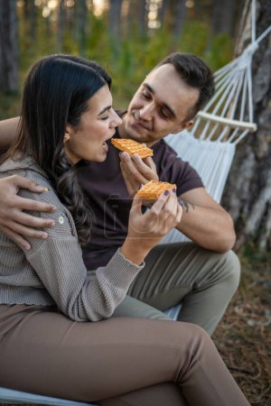 Téléchargez les photos : Couple adulte homme et femme amoureux manger gaufre dans le parc naturel ou les bois - en image libre de droit