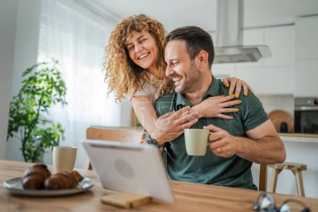 Photo for Happy couple caucasian adult man and woman husband and wife morning routine use digital tablet while have a cup of coffee or tea bonding and love at home bright photo copy space - Royalty Free Image