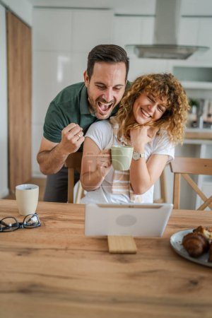 Photo for Happy couple caucasian adult man and woman husband and wife morning routine use digital tablet while have a cup of coffee or tea bonding and love at home bright photo copy space - Royalty Free Image