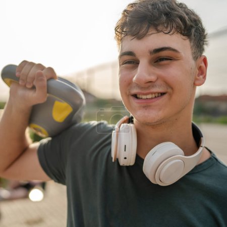 Photo for One man young caucasian male teenager stand outdoor in day training with russian bell girya kettlebell weight exercise real person copy space - Royalty Free Image