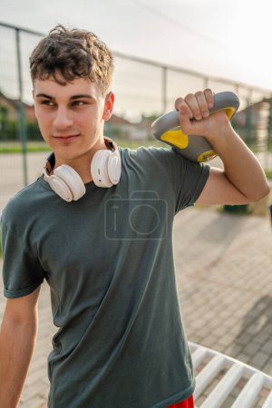 Foto de Un hombre joven caucásico adolescente pie al aire libre en el entrenamiento de día con campana rusa girya kettlebell peso ejercicio persona real copiar espacio - Imagen libre de derechos