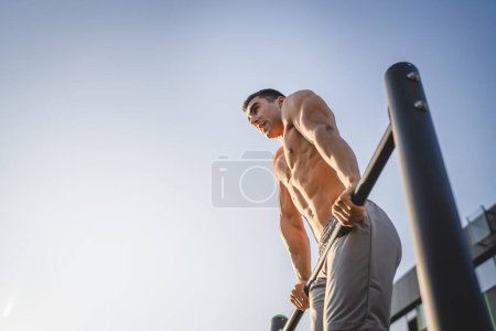 Photo for One man young adult caucasian male athlete training at outdoor open gym pull ups exercise healthy lifestyle and recreation training concept in the city in summer day real people copy space - Royalty Free Image