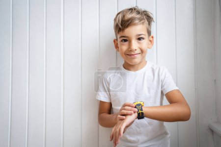 Téléchargez les photos : Caucasien garçon 7 ans mâle enfant utilisation montre intelligente à la maison - en image libre de droit