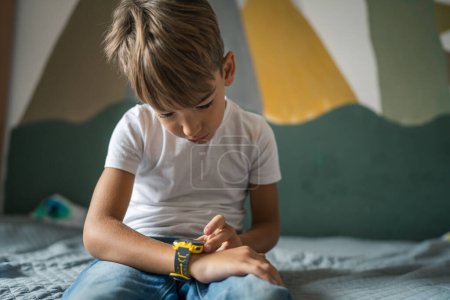 Foto de Niño caucásico 7 años niño varón uso reloj inteligente en casa - Imagen libre de derechos