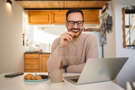 Photo for One man adult caucasian male sit at the table at home having breakfast with laptop computer prepare for work daily morning routine real people copy space - Royalty Free Image