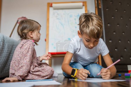 Foto de Un pequeño niño caucásico con hermana dibujar con crayón en casa - Imagen libre de derechos