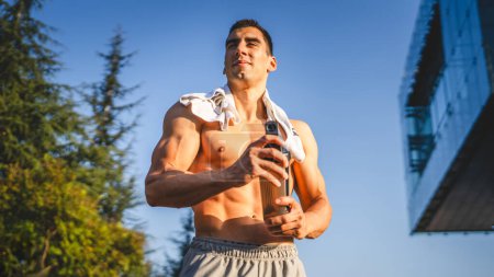 Téléchargez les photos : Un homme caucasien jeune athlète masculin prendre un frein pendant l'entraînement en plein air dans le parc salle de gym en plein air tenir shaker supplément dans la main heureux confiant espace de copie forte - en image libre de droit