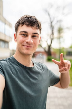Photo for One man young adult caucasian teenager stand outdoor posing self portrait selfie looking to the camera happy confident wear shirt casual real person copy space ugc user generated content - Royalty Free Image