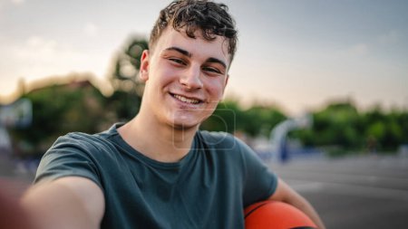 Téléchargez les photos : Un adolescent caucasien mâle caucasien jeune homme debout sur le terrain de basket-ball avec balle dans la soirée prêt à jouer copie espace de jeu personne réelle ugc utilisateur généré contenu autoportrait selfie - en image libre de droit