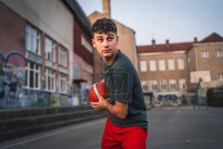 Foto de Un adolescente caucásico hombre caucásico joven de pie en la cancha de baloncesto con pelota en la noche listo para jugar espacio de copia juego persona real - Imagen libre de derechos